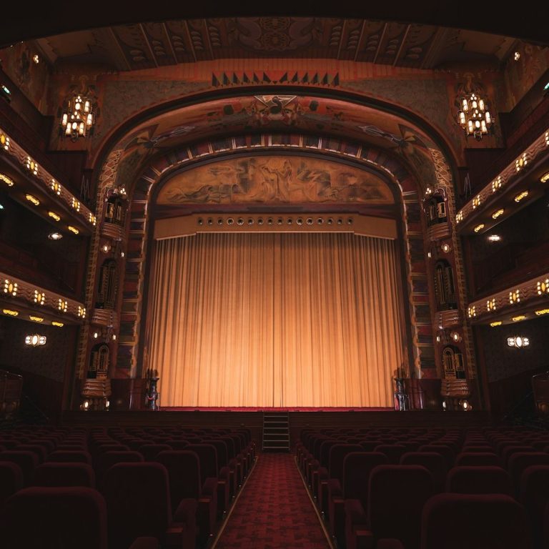 Sonderformen Leerer Theaterraum mit rotem Teppich und goldenen Vorhängen vor der Bühne.