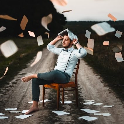 Ein Mann sitzt auf einem Stuhl auf einem Weg, umgeben von fliegenden Papierblättern.